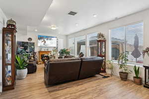 Living area with light wood finished floors, a warm lit fireplace, and visible vents