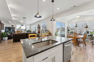 Kitchen with visible vents, light wood-style flooring, decorative light fixtures, white cabinetry, and a sink