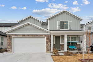 View of front of home featuring board and batten siding, concrete driveway, covered porch, and stone siding