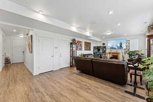 Living room featuring a warm lit fireplace, light wood-style flooring, recessed lighting, visible vents, and baseboards