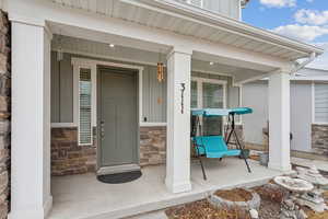 Entrance to property with covered porch, stone siding, and board and batten siding