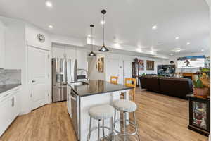 Kitchen with a breakfast bar area, dark countertops, light wood-style flooring, appliances with stainless steel finishes, and a sink