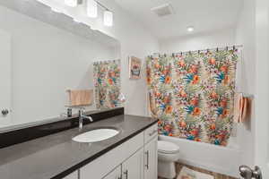 Bathroom with shower / tub combo with curtain, visible vents, toilet, vanity, and wood finished floors