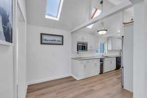 Kitchen featuring a skylight, stainless steel microwave, white cabinets, and a sink