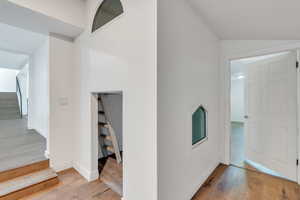 Hall with lofted ceiling, hardwood / wood-style flooring, stairs, and baseboards