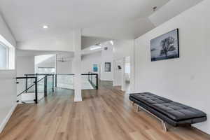 Hall featuring lofted ceiling, light wood-type flooring, baseboards, and an upstairs landing