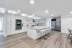 Kitchen with stainless steel appliances, a spacious island, a sink, wall chimney range hood, and decorative backsplash