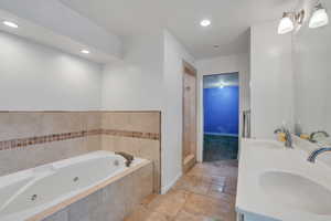 Full bath with a sink, a jetted tub, stone tile floors, and double vanity