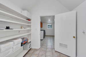 Kitchen featuring lofted ceiling, light tile patterned floors, visible vents, open shelves, and washer and clothes dryer