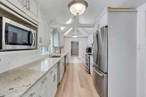 Kitchen with stainless steel appliances, white cabinetry, a sink, and backsplash