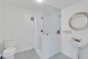 Bathroom featuring toilet, marble finish floor, baseboards, and a tile shower