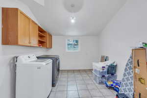 Laundry room featuring separate washer and dryer, light tile patterned flooring, cabinet space, and baseboards