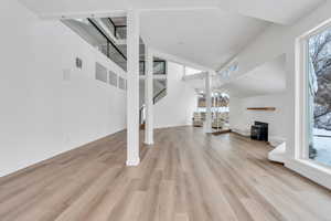 Unfurnished living room featuring visible vents, stairway, light wood-style floors, a wood stove, and high vaulted ceiling