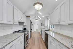 Kitchen with stainless steel appliances, lofted ceiling with skylight, white cabinets, a sink, and under cabinet range hood