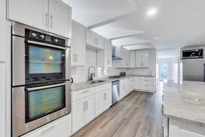 Kitchen featuring stainless steel appliances, tasteful backsplash, a sink, wall chimney range hood, and light stone countertops