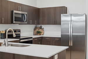 Kitchen with stainless steel appliances, dark wood style cabinets, tile backsplash and quartz counters
