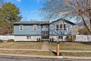 Raised ranch featuring a front yard, brick siding, and fence