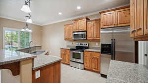 Kitchen featuring crown molding, a sink, stainless steel appliances, light stone countertops, and decorative light fixtures