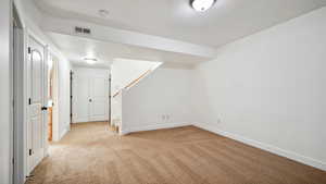 Basement featuring stairs, light colored carpet, baseboards, visible vents, and a textured ceiling