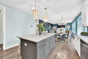 Kitchen with light stone counters, a center island, gray cabinetry, light wood-style floors, and stainless steel dishwasher