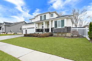 View of front facade with a garage, fence, stone siding, driveway, and a front yard