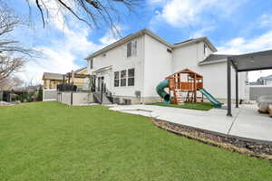 Back of house featuring a playground, a yard, fence, and stucco siding