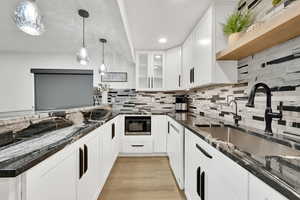 Kitchen with black microwave, open shelves, dark stone countertops, and a sink