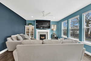 Living area with ceiling fan, visible vents, baseboards, dark wood-style floors, and a glass covered fireplace