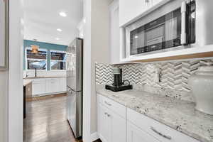 Kitchen with hardwood / wood-style flooring, light stone counters, freestanding refrigerator, white cabinetry, and backsplash