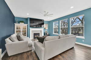 Living area with dark wood-style floors, recessed lighting, a glass covered fireplace, ceiling fan, and baseboards