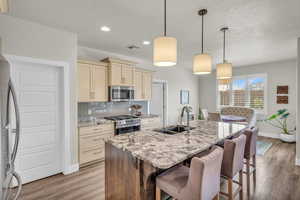 Kitchen featuring tasteful backsplash, appliances with stainless steel finishes, cream cabinets, a kitchen bar, and a sink