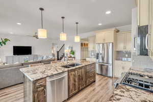 Kitchen with cream cabinets, stainless steel appliances, a sink, open floor plan, and light wood-type flooring