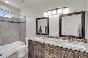 Full bathroom featuring toilet, double vanity, visible vents, and a sink