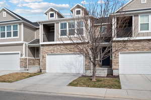 Multi unit property featuring an attached garage, a balcony, stone siding, and concrete driveway