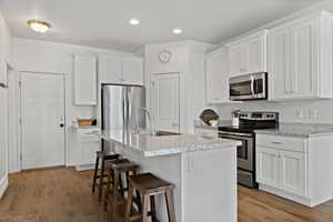 Kitchen featuring a breakfast bar, a sink, white cabinets, appliances with stainless steel finishes, and light wood finished floors