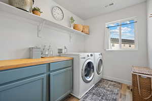 Washroom featuring cabinet space, visible vents, baseboards, light wood-style floors, and washing machine and dryer