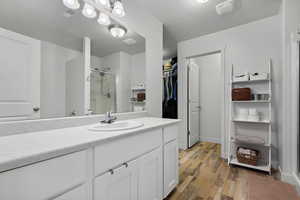 Bathroom featuring visible vents, a spacious closet, a stall shower, vanity, and wood finished floors