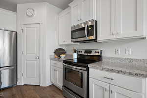 Kitchen with stainless steel appliances, dark wood-type flooring, white cabinetry, and light stone counters