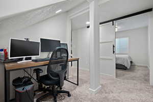 Office space featuring a barn door, baseboards, carpet, vaulted ceiling, and a textured ceiling
