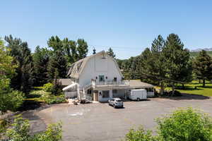 View of front of property featuring stairs, a gambrel roof, uncovered parking, a wooden deck, and view of scattered trees