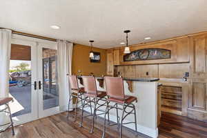 Kitchen featuring a breakfast bar, french doors, pendant lighting, dark countertops, and dark wood-type flooring