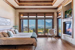 Bedroom featuring a raised ceiling, hardwood / wood-style floors, access to outside, crown molding, and a mountain view