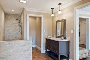 Bathroom featuring a textured ceiling, vanity, baseboards, ornamental molding, and tiled shower