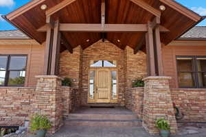 View of exterior entry with stone siding and a shingled roof