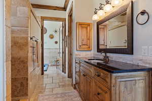 Bathroom with tile walls, stone tile flooring, ornamental molding, wainscoting, and vanity