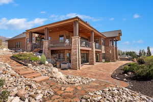 Back of property with stone siding, a patio, and a balcony