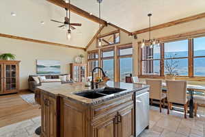 Kitchen featuring beam ceiling, stone tile flooring, stainless steel dishwasher, a sink, and high vaulted ceiling