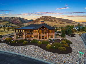 Back of house at dusk featuring a chimney, stone siding, a mountain view, and a balcony