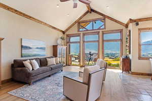 Living room featuring light wood finished floors, baseboards, a textured wall, beamed ceiling, and high vaulted ceiling