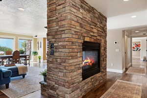 Unfurnished living room featuring a textured ceiling, recessed lighting, wood finished floors, a multi sided fireplace, and baseboards